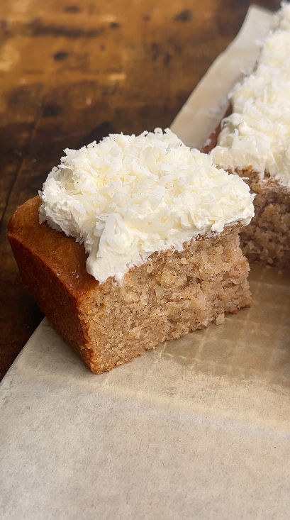 "A slice of vegan coconut cake topped with dairy-free whipped cream and coconut flakes"