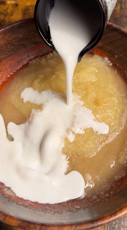 "Coconut milk being poured into a mixing bowl with applesauce and wet ingredients for vegan coconut cake"