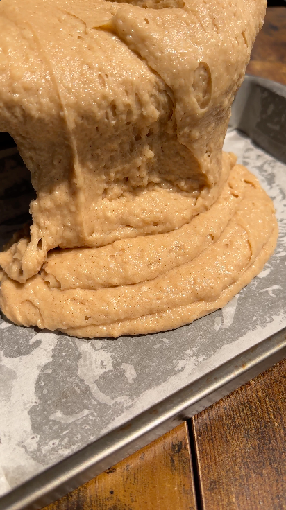 "Thick vegan coconut cake batter being poured into a parchment-lined baking pan"