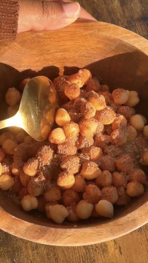 Chickpeas being tossed with Cajun spices in a wooden bowl with a gold spoon