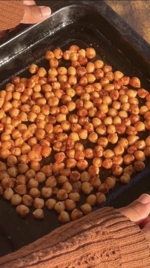 Seasoned chickpeas spread on a dark baking tray ready for the air fryer